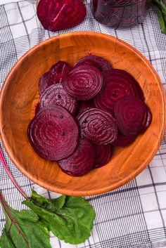 a wooden bowl filled with sliced beets on top of a checkered table cloth