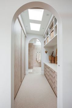 an arched doorway leads to a walk - in closet with white walls and beige carpet