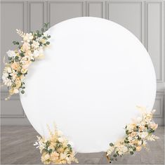 a large round white sign with flowers on it's sides and greenery around the edges