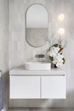 a white sink sitting under a mirror next to a vase with flowers in front of it