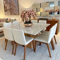 a dining room table with white chairs and flowers on the centerpiece in front of it