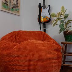 an orange velvet bean bag chair next to a guitar