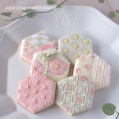 four decorated cookies sitting on top of a white plate next to green leaves and flowers