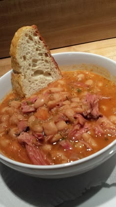 a bowl of beans and ham soup with a piece of bread sticking out of it