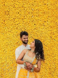 a man and woman standing next to each other in front of a yellow flower wall