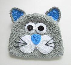 a crocheted gray cat hat with blue eyes and ears is shown on a white surface