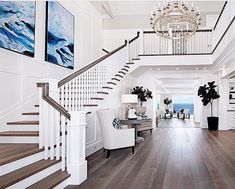 a large foyer with white walls and wood flooring, chandelier and paintings on the wall