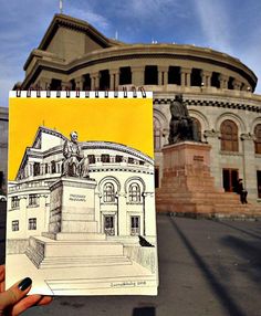 a person holding up a drawing in front of a building with a statue on it