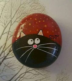 a painted rock with a black cat on it's face and trees in the background