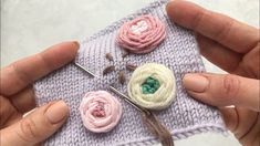 two hands are holding small crocheted flowers on a piece of cloth with needles