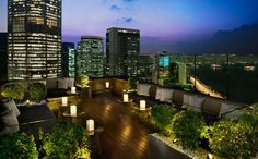 an outdoor deck with chairs and lights in the city at night, surrounded by tall buildings