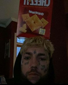 a man with tattoos on his face standing in front of a box of cheez it