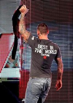 a man holding up a black tie in front of a large screen with the words best in the world on it