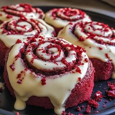 several red velvet rolls with white frosting on a black plate and sprinkles