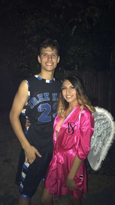 a man and woman dressed in costumes posing for a photo together at night with angel wings