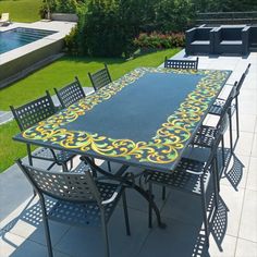 an outdoor dining table with chairs around it in front of a swimming pool and landscaping area