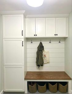 a white mud room with wooden bench and storage bins