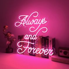 a neon sign that says always and forever with books in front of it on a table