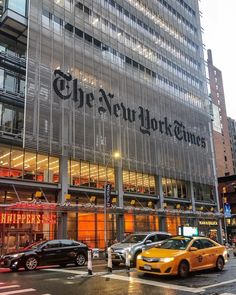 the new york times building is lit up at night with cars parked on the street