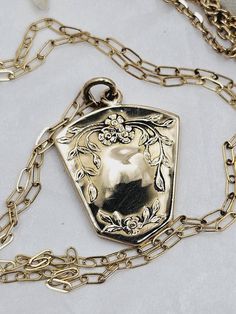 This is a "once in a lifetime" piece of estate jewelry.  This would make a lovely, thoughtful gift for your sweetheart. This very special antique locket necklace is made of highly polished solid yellow gold.  The locket is 10K and the chain is 14K.  Both are stamped accordingly. The locket has a unique shield shape which has a beautiful floral forget-me-not design on the front and a monogram on the back.  The locket is a little over one inch long.  The inside still holds the original black and white portrait of a handsome gentleman.  The photo is held in place by the original frame and cover.  I imagine there is a wonderful love story attached to this piece.  The necklace is a mini paperclip style chain with a spring ring clasp.  The clasp is stamped 585 (14K).  The chain is 18 inches long Victorian Jewelry In 14k Gold With Hallmark, Formal Heirloom Necklace Stamped 14k, Victorian 14k Gold Jewelry With Hallmark, Vintage Charm Jewelry For Valentine's Day Formal, Vintage Charm Jewelry For Valentine's Day Formal Occasion, Elegant Brass Necklaces For Valentine's Day, Formal Vintage Charm Jewelry For Valentine's Day, Vintage Rose Gold Necklaces For Mother's Day, Vintage Rose Gold Necklace For Mother's Day