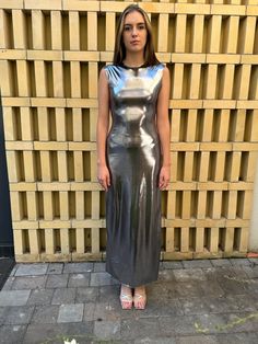 a woman standing in front of a brick wall wearing a metallic dress and pink sandals