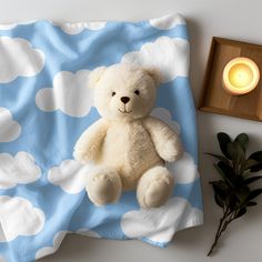 a white teddy bear sitting on top of a blue and white blanket next to a candle