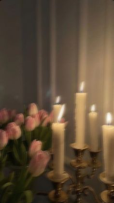 a bunch of lit candles sitting next to each other in front of a wall with flowers