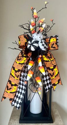 a halloween decoration on top of a white vase with candy corn and black and orange decorations