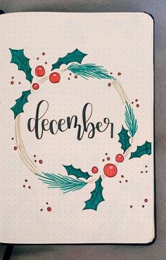 a notebook with the word december written on it and holly wreath around the corner, surrounded by red berries