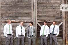 a group of men standing next to each other in front of a wooden wall wearing ties