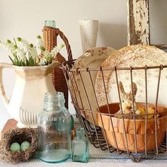 there is a basket with eggs in it next to other items and vases on the table