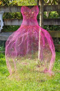 a pink mesh dress sitting on top of a lush green field next to a wooden fence