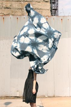 a woman is holding up a blue and white tie - dyed cloth over her head