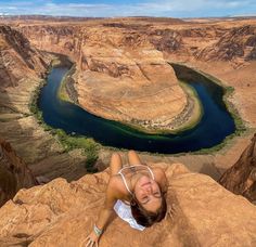 a woman laying on top of a cliff next to a river