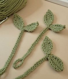 two crocheted flowers sitting on top of a table next to a ball of yarn