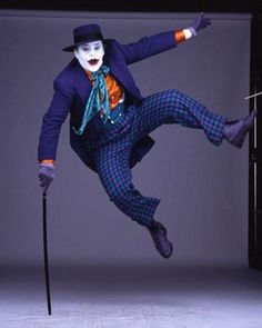 a man dressed as the joker jumping in the air with his legs spread out and holding an umbrella