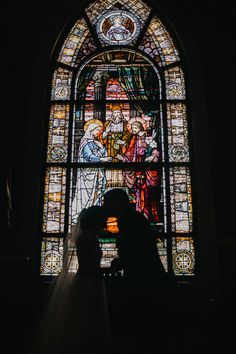 a bride and groom standing in front of a stained glass window