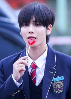 a young man wearing a suit and tie holding a lollipop in his mouth