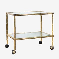 a gold bamboo and glass bar cart with wheels on the bottom, one shelf is empty