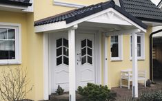 a small yellow house with white trim and windows on the front door, next to a bench