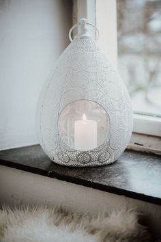 a white vase sitting on top of a window sill with a lit candle in it