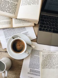 an open laptop computer sitting on top of a wooden table next to books and cups of coffee