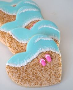 three decorated cookies with pink and blue icing on white table top, one in the shape of a beach scene