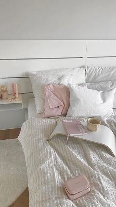 a white bed topped with pillows and a pink book on top of it next to a night stand