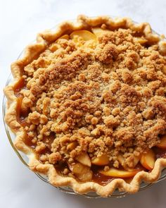 an apple pie with crumbs on top sits in a glass dish, ready to be eaten