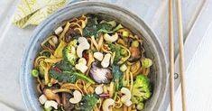 a bowl filled with noodles, broccoli and mushrooms next to chopsticks