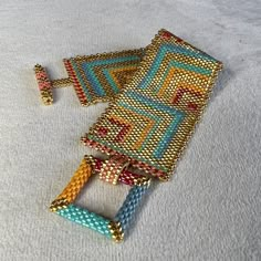 two pieces of beaded jewelry laying on top of a white cloth covered floor next to each other