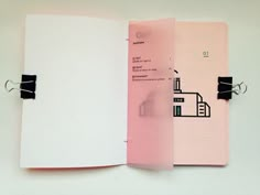 an open pink notebook with black clips attached to the front and back pages, sitting on a white surface