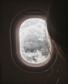 a woman looking out an airplane window at the clouds