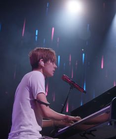 a young man sitting at a piano in front of a microphone on stage with lights behind him